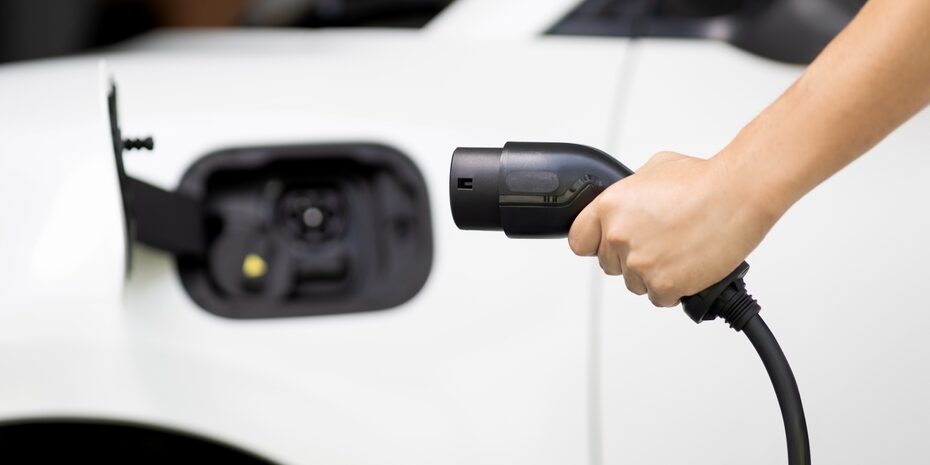 Focus,Hand,Holding,Ev,Charger,Plug,With,Blurred,Background,Of